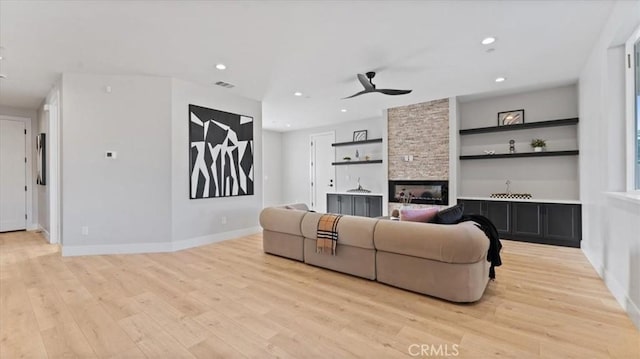 living room featuring built in features, a fireplace, light hardwood / wood-style floors, and ceiling fan