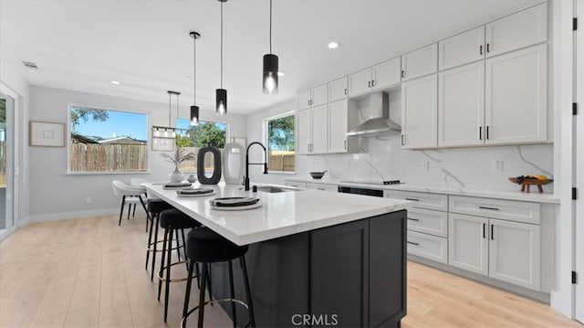 kitchen featuring wall chimney exhaust hood, sink, a center island with sink, and white cabinets