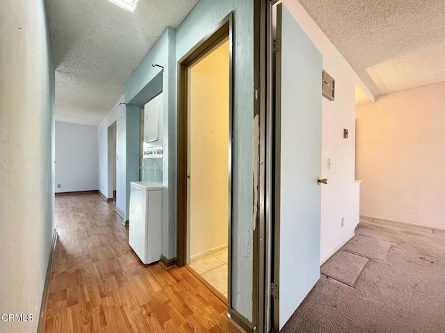 hallway featuring washer / clothes dryer, a textured ceiling, and light hardwood / wood-style flooring