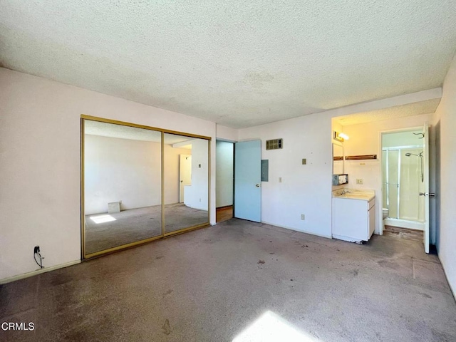 unfurnished bedroom featuring ensuite bathroom, light carpet, a textured ceiling, a closet, and washer and clothes dryer