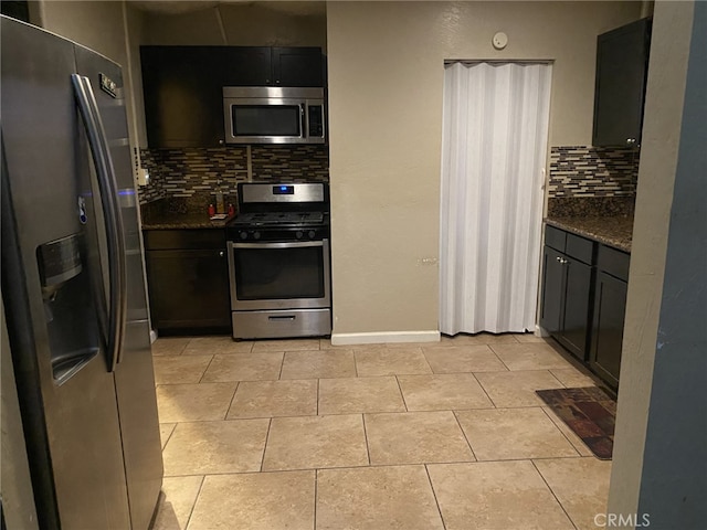 kitchen featuring light tile patterned floors, tasteful backsplash, baseboards, dark stone counters, and stainless steel appliances