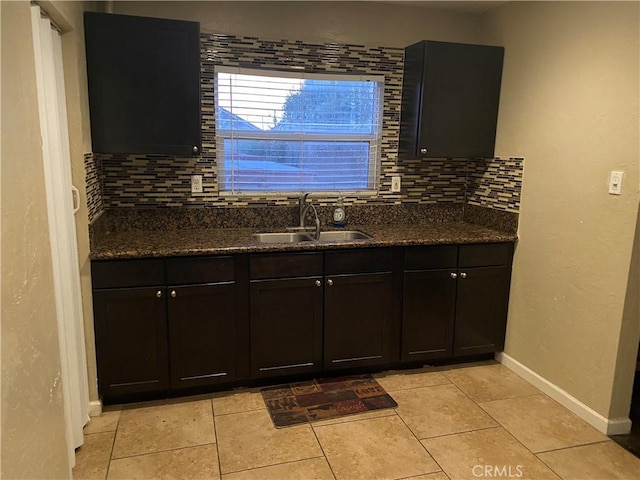 kitchen with light tile patterned floors, decorative backsplash, a sink, dark stone counters, and baseboards