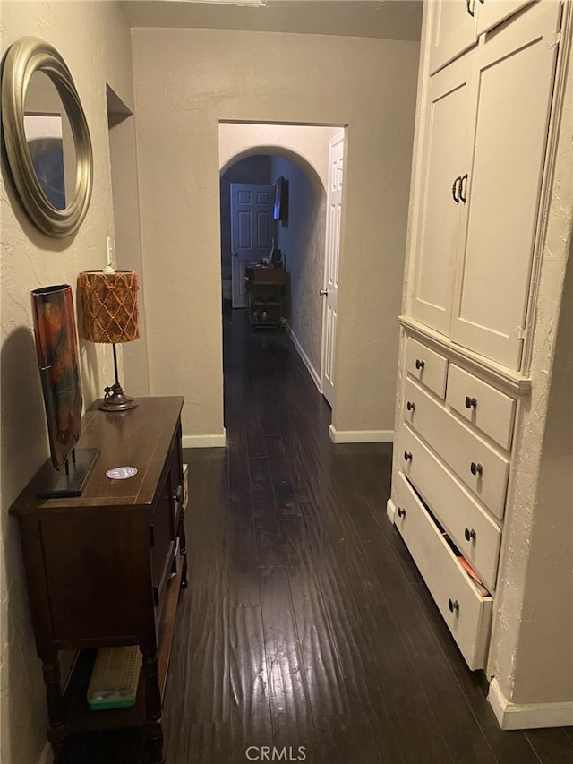 corridor with dark wood-type flooring, arched walkways, a textured wall, and baseboards