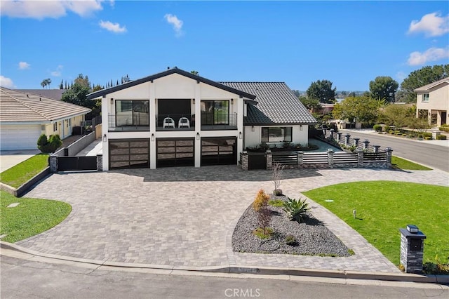 view of front of home featuring a balcony, an attached garage, fence, decorative driveway, and stucco siding