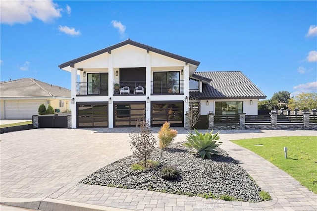 view of front of house with an attached garage, a balcony, fence, decorative driveway, and stucco siding