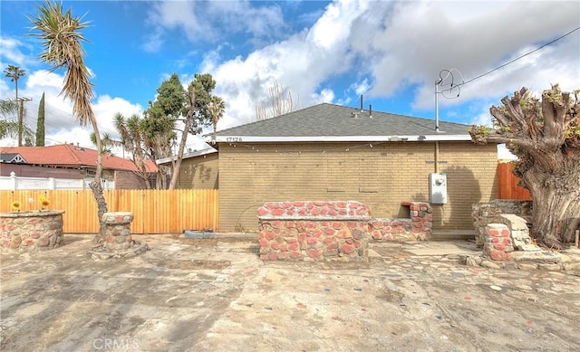 view of home's exterior with brick siding, a patio area, roof with shingles, and fence