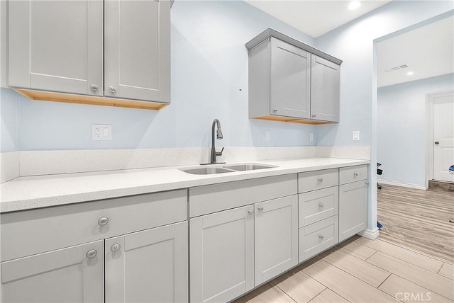 kitchen with wood tiled floor, gray cabinetry, visible vents, a sink, and light countertops