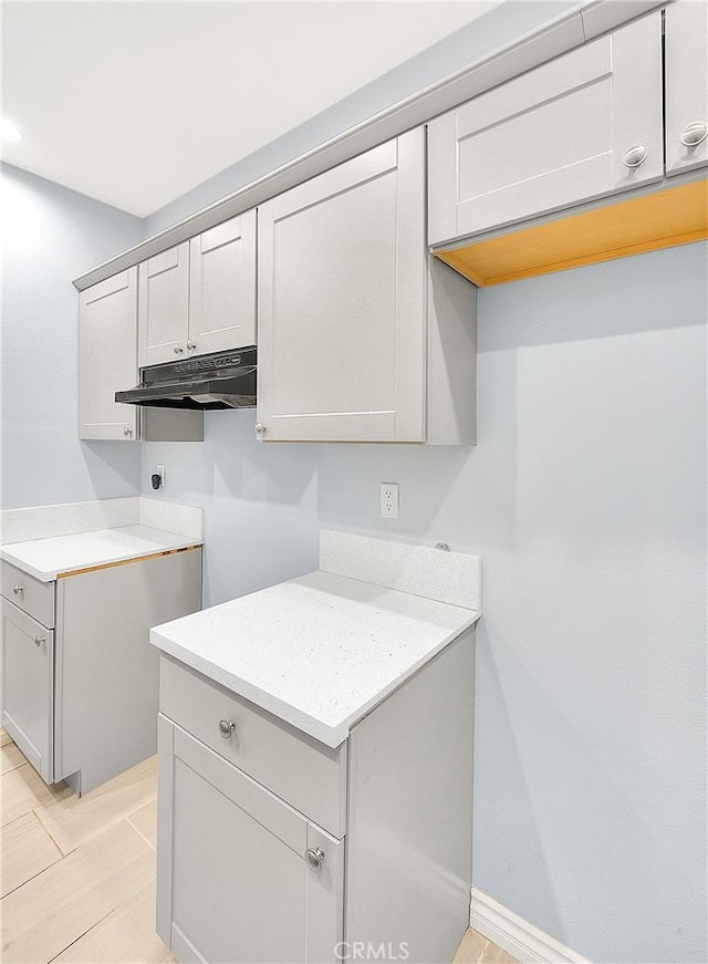 kitchen with light tile patterned floors, under cabinet range hood, and gray cabinets