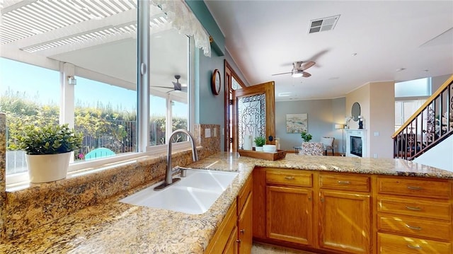 kitchen featuring sink, light stone counters, ceiling fan, and kitchen peninsula