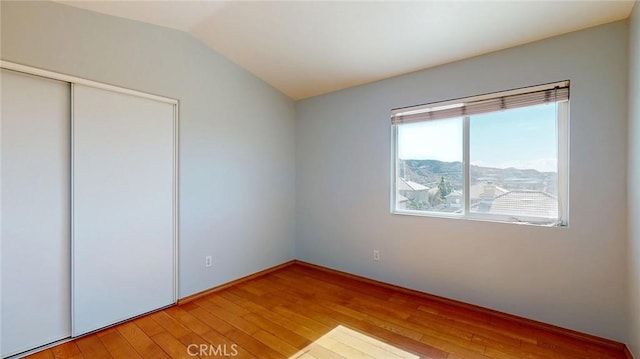 unfurnished bedroom with lofted ceiling, a mountain view, hardwood / wood-style floors, and a closet