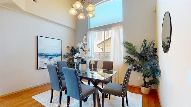 dining room featuring wood-type flooring, a towering ceiling, and a notable chandelier