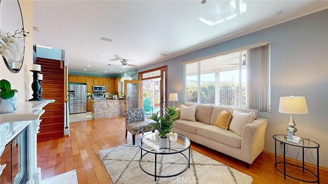 living room with light hardwood / wood-style flooring, a premium fireplace, and ceiling fan