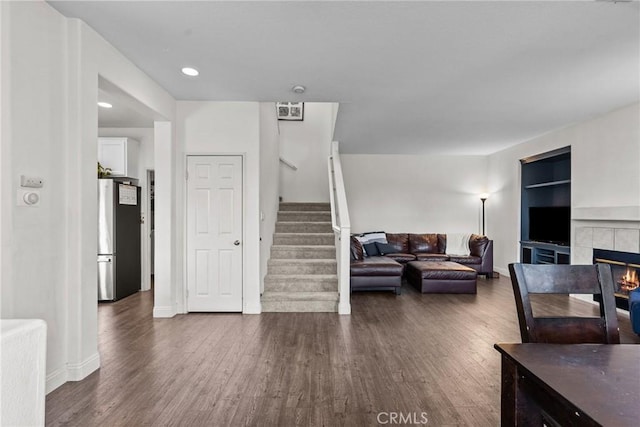 living room featuring built in shelves, stairs, dark wood finished floors, and a fireplace