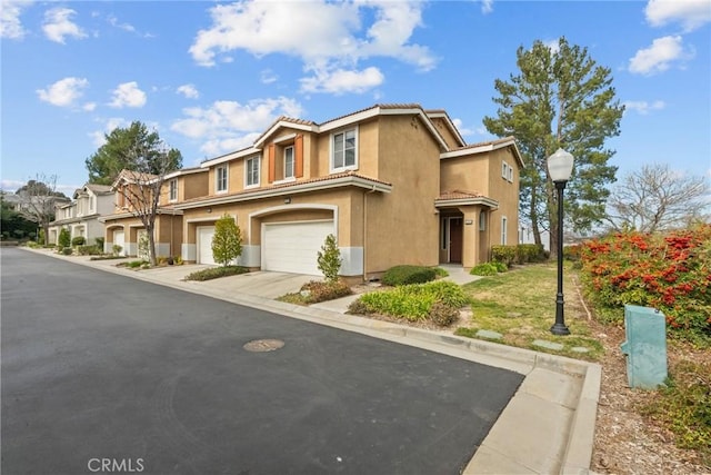 multi unit property with an attached garage, a tile roof, driveway, a residential view, and stucco siding