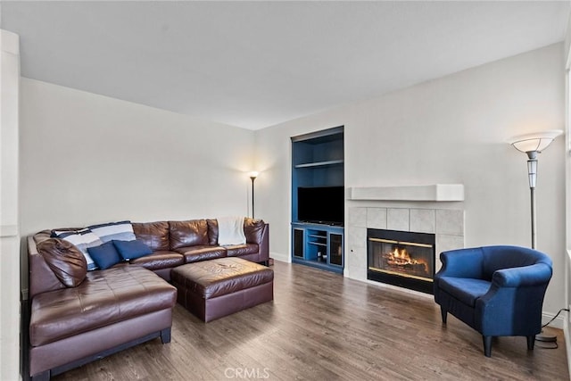 living room featuring built in shelves, a tile fireplace, baseboards, and wood finished floors