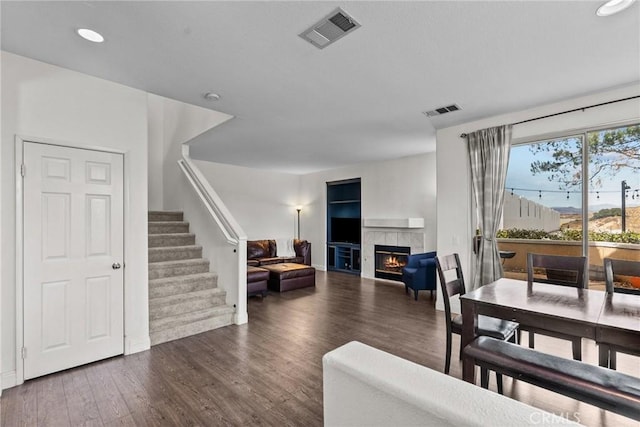 living room featuring stairway, a fireplace, visible vents, and dark wood-style flooring