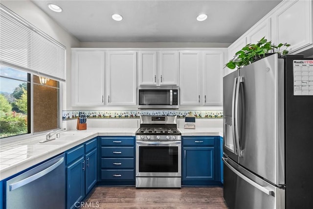 kitchen with appliances with stainless steel finishes, light countertops, a sink, and blue cabinetry