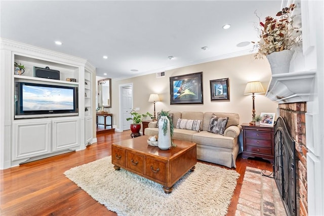 living area with light wood-style floors, a brick fireplace, recessed lighting, and crown molding