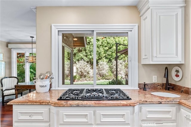 kitchen featuring hanging light fixtures, white cabinets, a sink, black gas stovetop, and light stone countertops