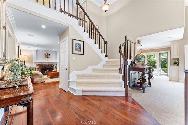 foyer featuring wood finished floors, a towering ceiling, stairway, a brick fireplace, and an inviting chandelier