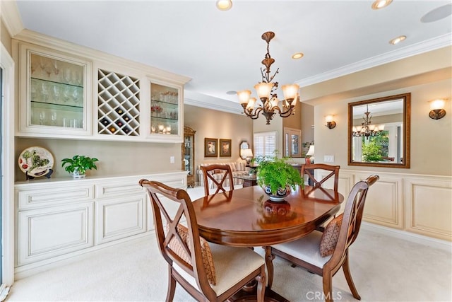 dining area featuring crown molding, a wainscoted wall, an inviting chandelier, and light colored carpet