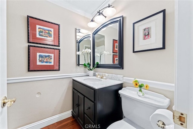 half bath featuring baseboards, toilet, wood finished floors, crown molding, and vanity