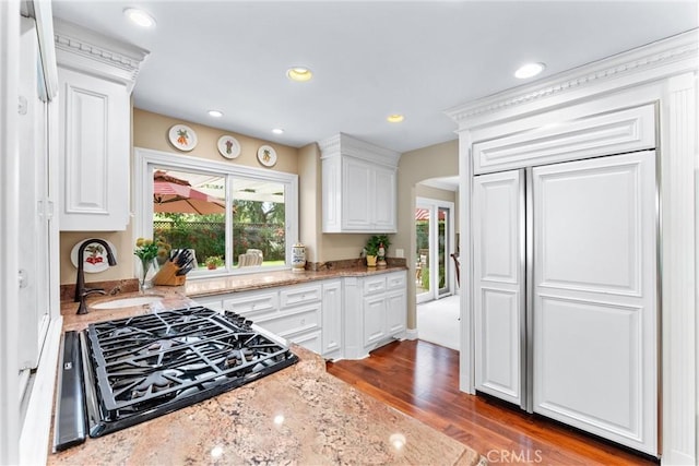 kitchen with arched walkways, white cabinets, light stone countertops, gas cooktop, and a sink