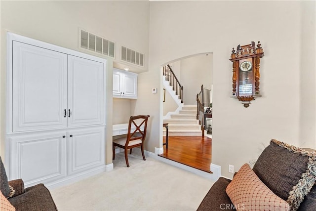 living area with arched walkways, light carpet, stairs, and visible vents