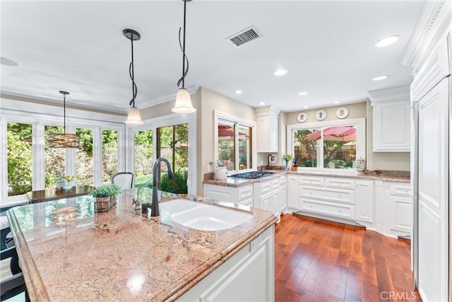 kitchen with hanging light fixtures, light stone counters, a sink, and visible vents