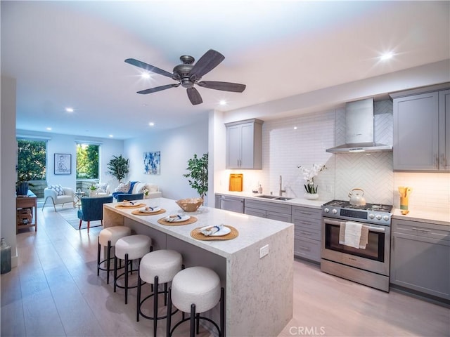 kitchen featuring appliances with stainless steel finishes, sink, gray cabinetry, wall chimney exhaust hood, and a breakfast bar area