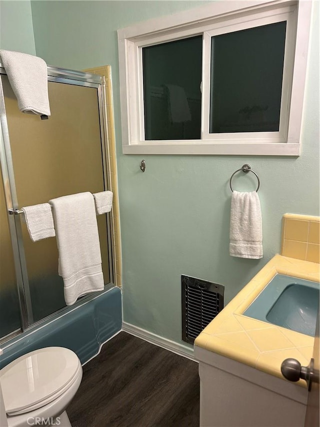 full bathroom featuring sink, hardwood / wood-style flooring, enclosed tub / shower combo, and toilet