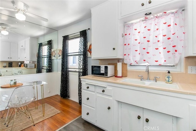 kitchen featuring white microwave, tasteful backsplash, wood finished floors, white cabinetry, and a sink