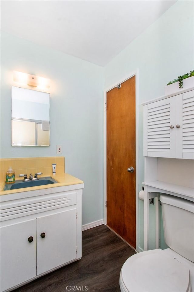 half bath featuring baseboards, toilet, wood finished floors, and vanity