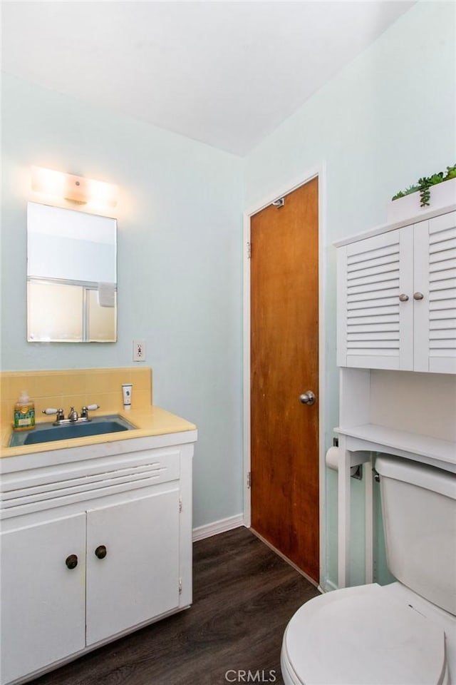 half bath with toilet, vanity, and wood finished floors