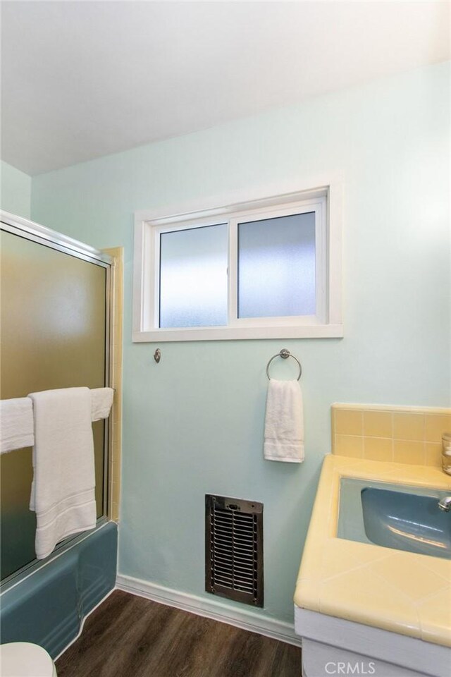 full bath featuring toilet, visible vents, wood finished floors, vanity, and enclosed tub / shower combo