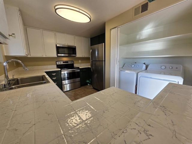 kitchen featuring stainless steel appliances, a sink, white cabinets, light countertops, and independent washer and dryer