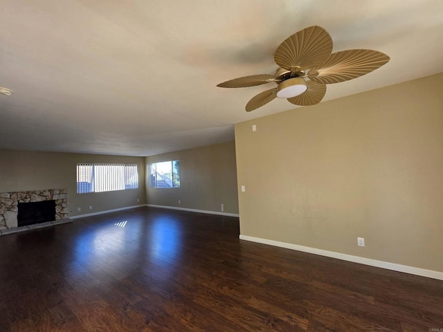 unfurnished living room featuring ceiling fan, a fireplace, baseboards, and dark wood finished floors