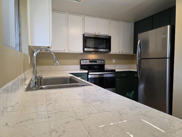 kitchen with stainless steel appliances, light countertops, white cabinetry, a sink, and dark cabinets