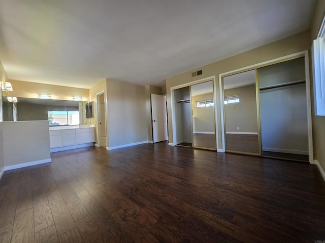 unfurnished bedroom featuring connected bathroom, visible vents, baseboards, dark wood-style floors, and two closets