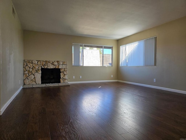 unfurnished living room with dark wood finished floors, a stone fireplace, and baseboards