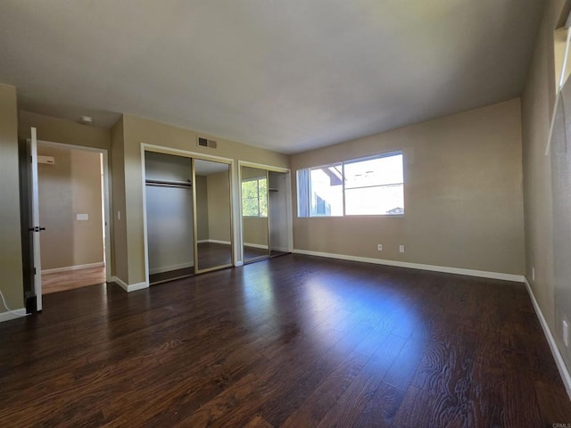 unfurnished bedroom featuring dark wood-style floors, visible vents, baseboards, and two closets