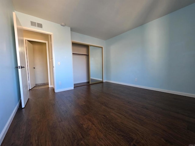 unfurnished bedroom with dark wood-style flooring, a closet, visible vents, and baseboards