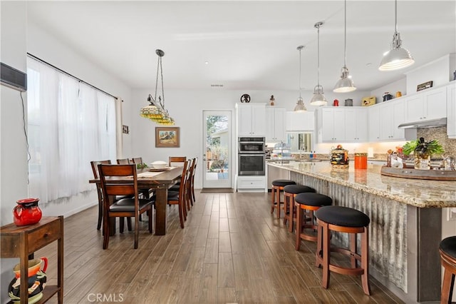 dining room featuring white cabinetry, dark hardwood / wood-style floors, a kitchen breakfast bar, and decorative light fixtures