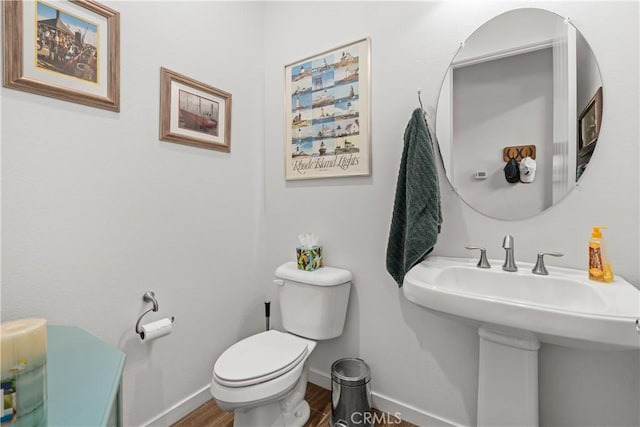 bathroom featuring toilet, a sink, baseboards, and wood finished floors