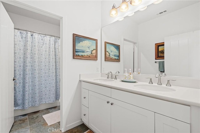 full bath with double vanity, a sink, stone finish flooring, and visible vents