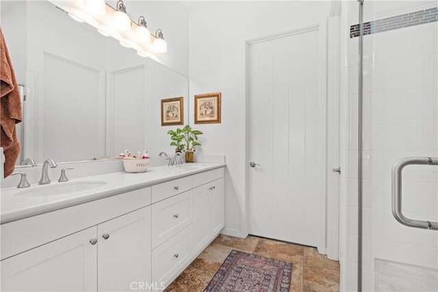 bathroom featuring double vanity, a tile shower, stone finish flooring, and a sink