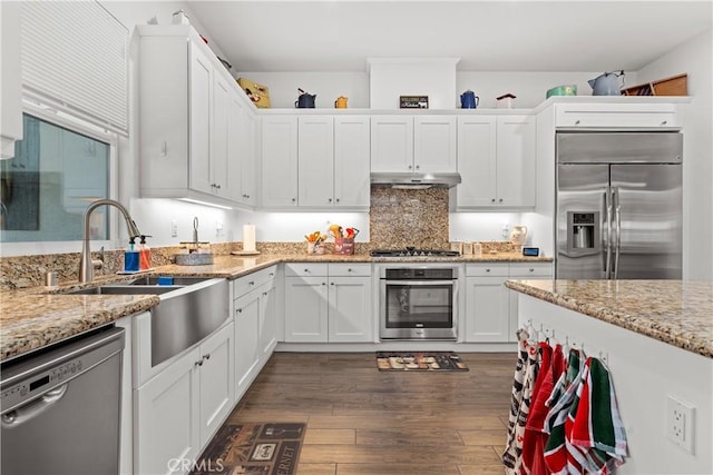 kitchen with stainless steel appliances, light stone counters, white cabinets, and dark hardwood / wood-style flooring