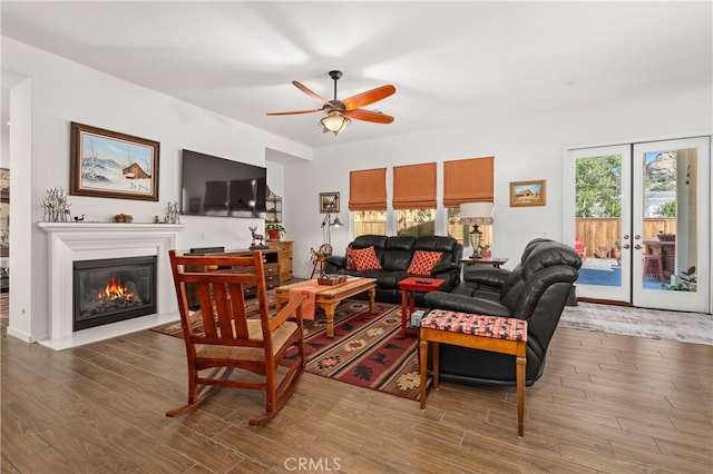 living room featuring wood finished floors, a glass covered fireplace, and a ceiling fan