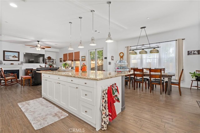 kitchen with light wood-type flooring, a kitchen island, light stone counters, white cabinets, and pendant lighting