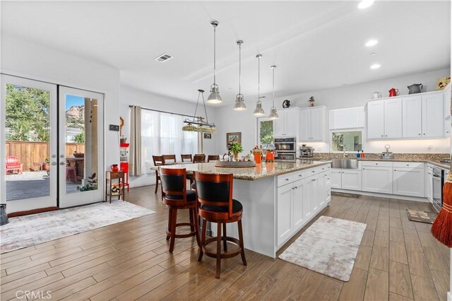 kitchen featuring a sink, a kitchen island, wood finished floors, visible vents, and white cabinets